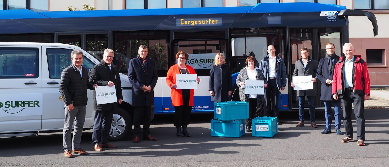 Rüdiger Krenkel KVG, Kreisbeigeordneter Winfried Ottmann, Martin Berg Vorstandsvorsitzender BWMK, Erste Kreisbeigeordnete Susanne Simmler, Katrin Hess Amt 70, Sabine Jennert SPESSARTregional, Dr. Christoph Heim BWMK, Markus Ewald RVMK, Oliver Habekost RVMK, Bürgermeister Rainer Schreiber Vorsitzender SPESSARTregional stehen vor den mit "Cargosurfer" beschrifteten Bussen